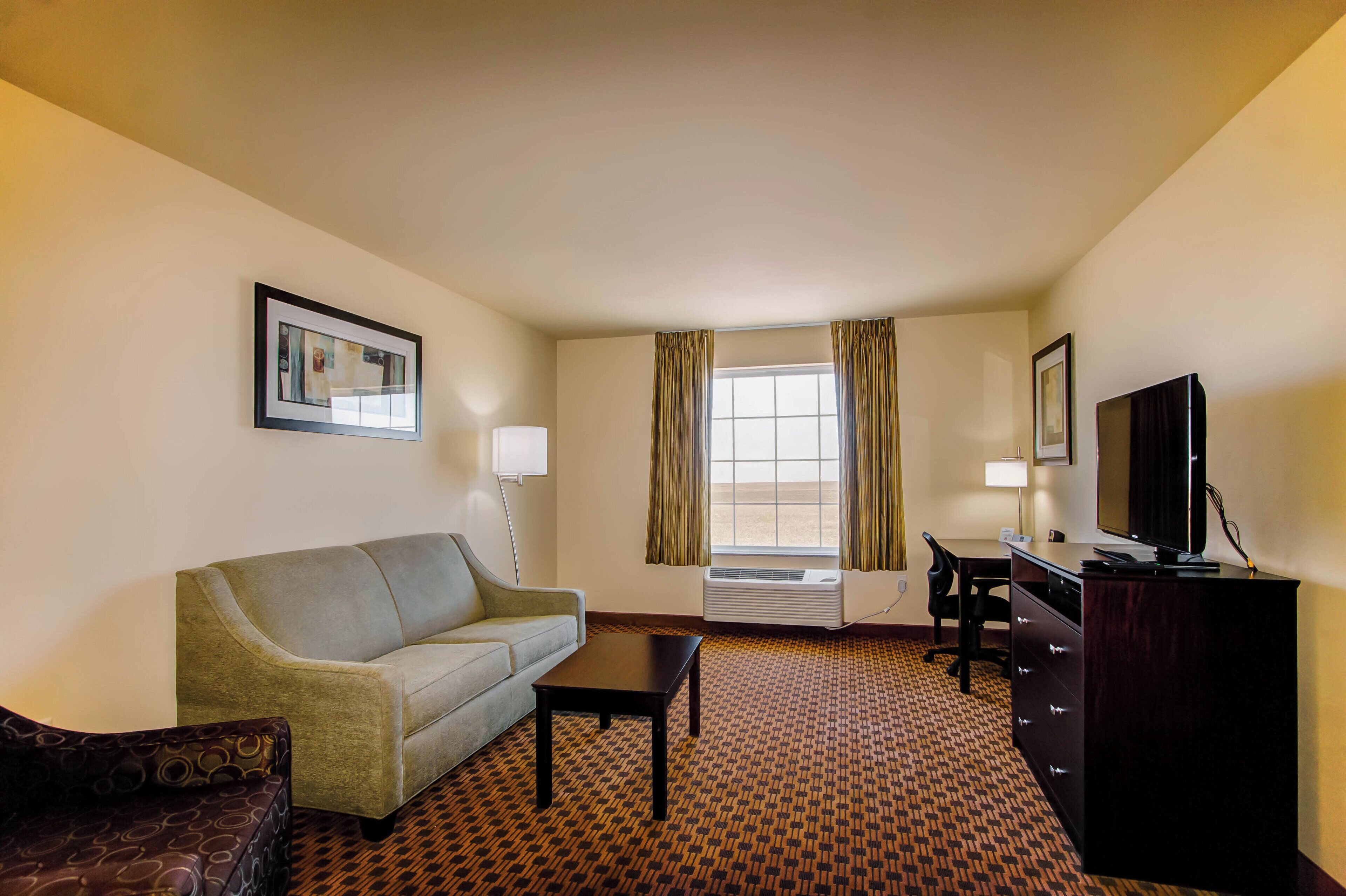 A hotel room with a sofa, a desk, a television, and a window with curtains.