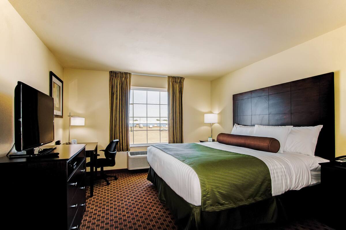 A hotel room with a bed, desk, chair, TV, and a window with curtains.