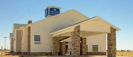 A building with a sign reading "Cobblestone Inn & Suites." It features a covered entrance with stone pillars and a flat roof.