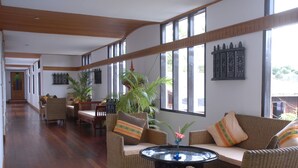 A spacious lobby with wicker furniture, large windows, and a central round table.