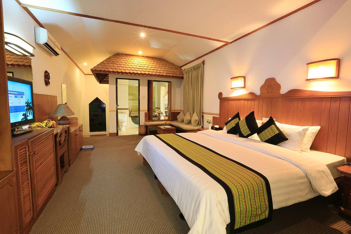 A hotel room with a large bed, a desk with a lamp, a television, and a view of the outside.