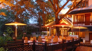 An outdoor dining area with tables and chairs, surrounded by a wooden fence, and illuminated by warm lighting.
