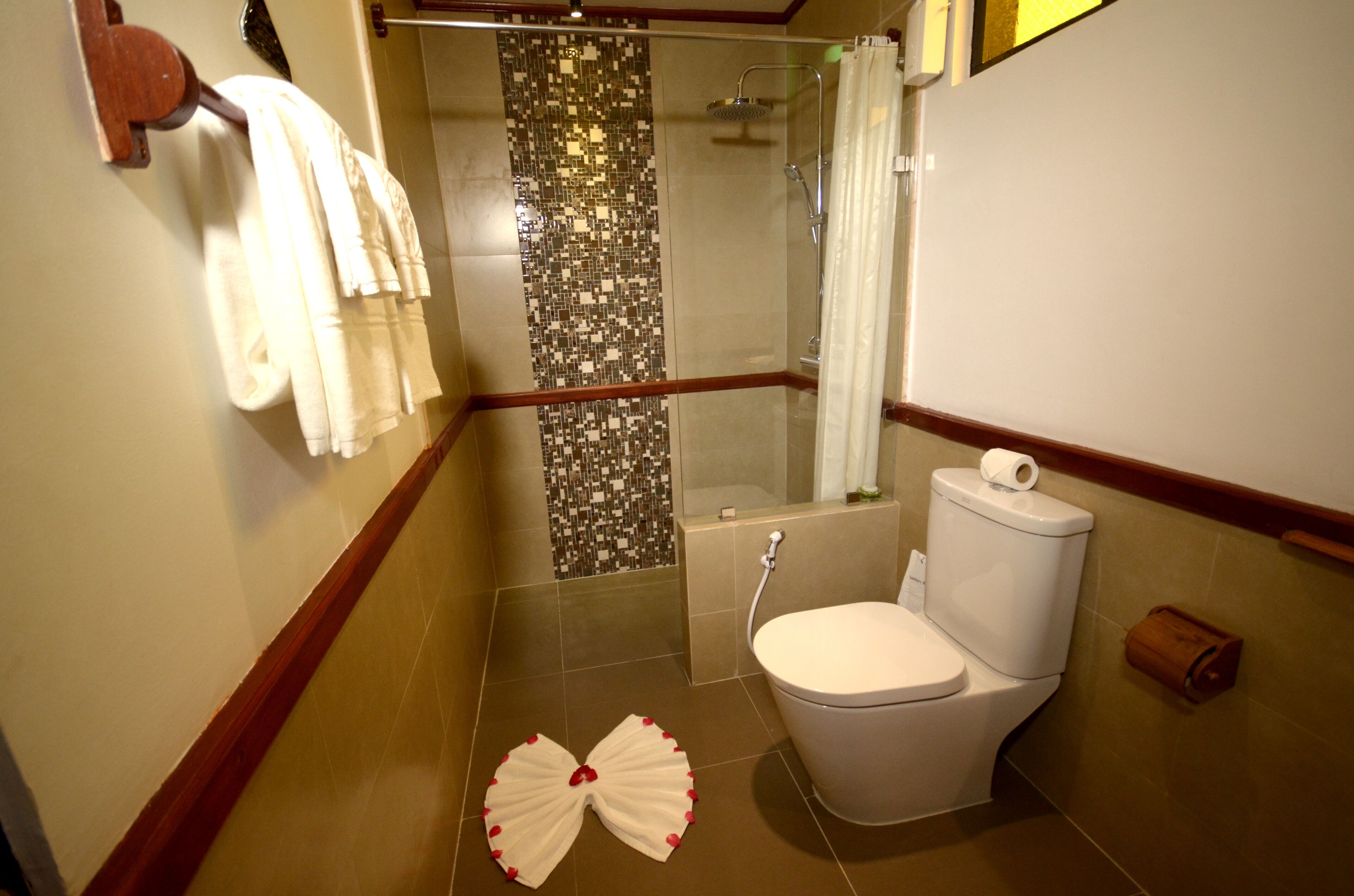 A bathroom with a toilet, shower, and a towel rack with multiple towels.