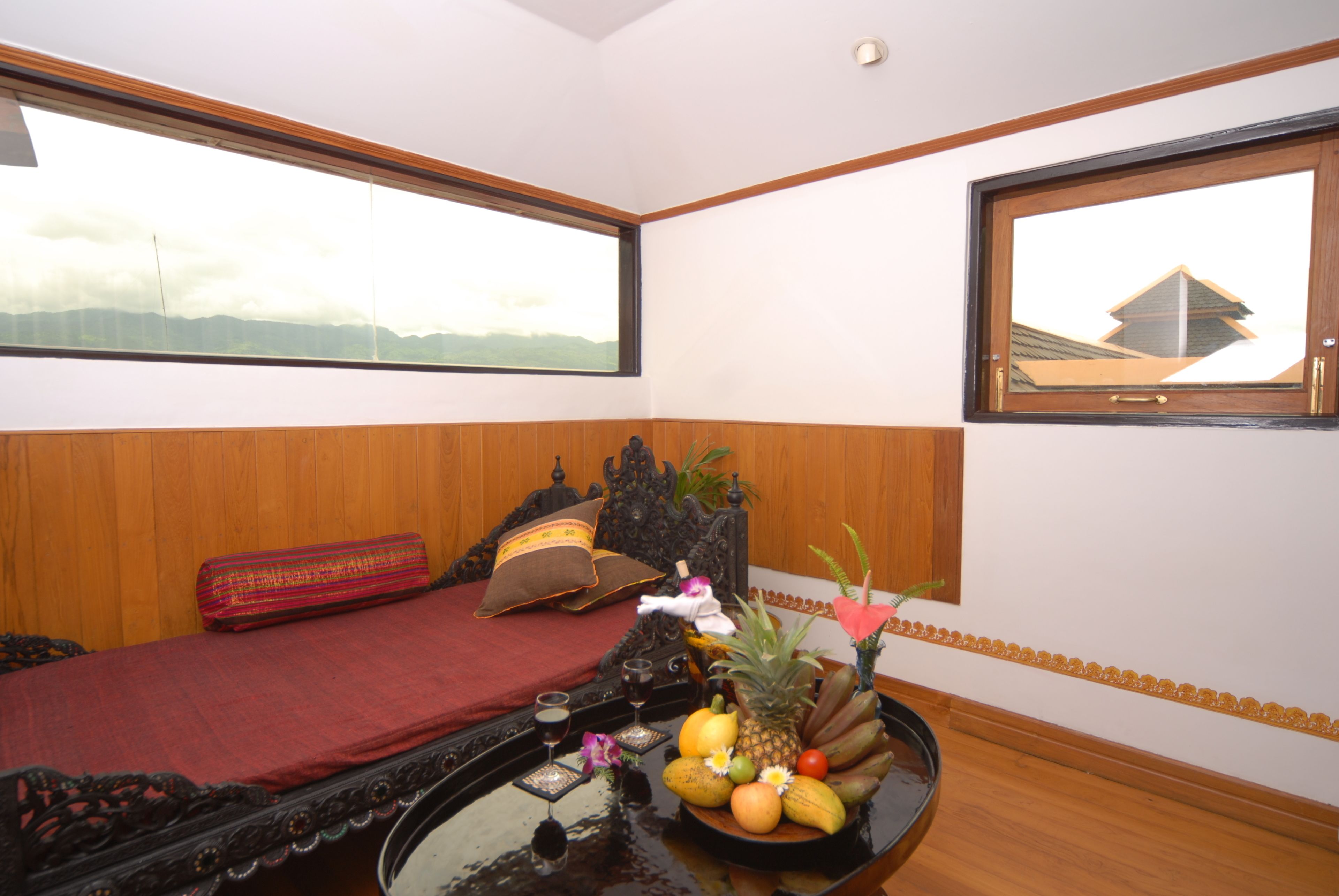 Une pièce comprenant un lit, une table avec des fruits et un objet décoratif, et offrant une vue sur les montagnes par une fenêtre.