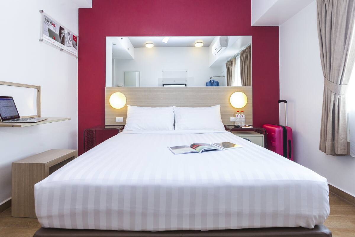 Una habitación de hotel con una cama grande, un escritorio con una computadora portátil, un espejo y una pared de acento roja.