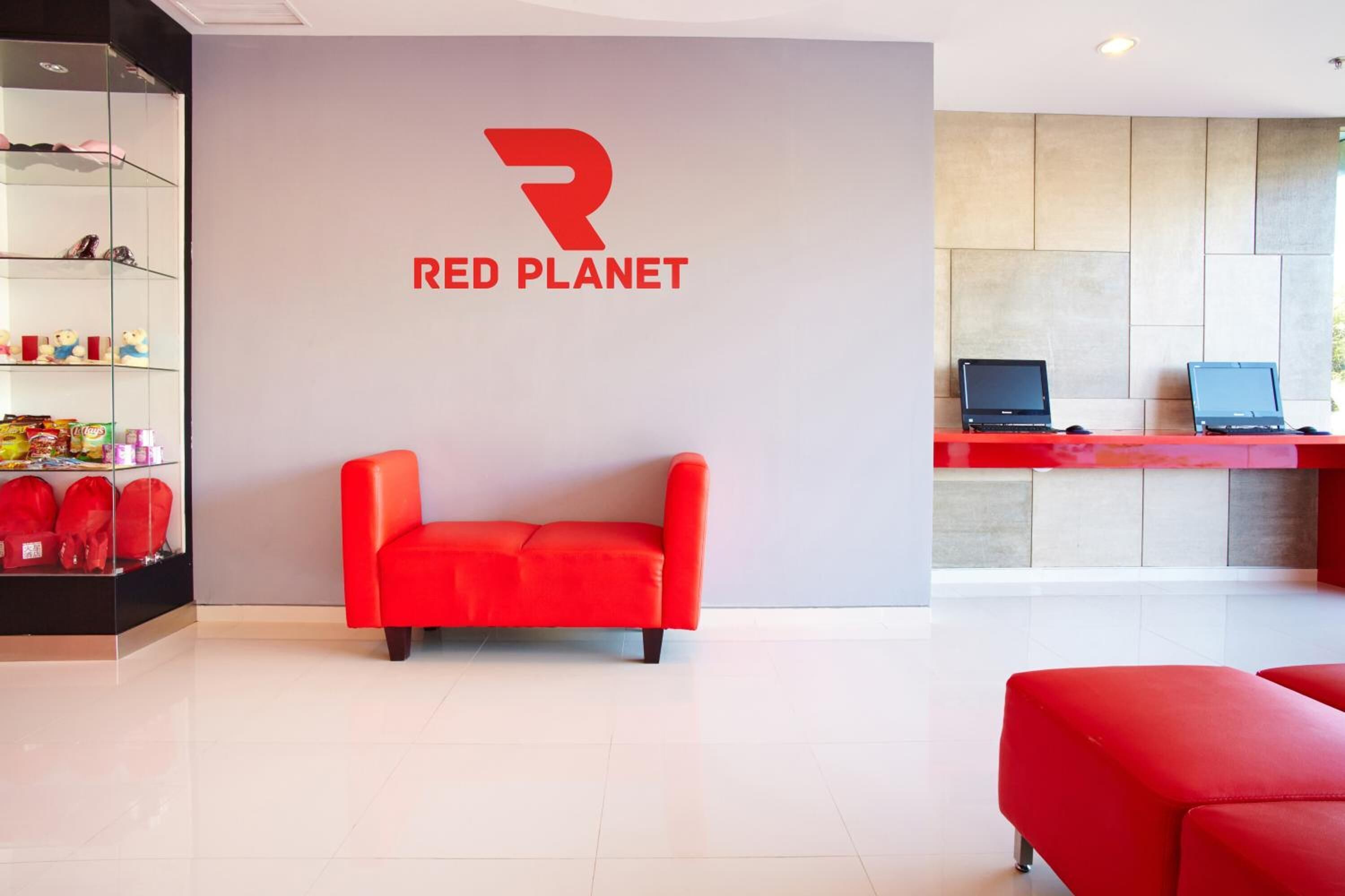 Un área de recepción moderna con un sofá rojo, una vitrina de vidrio con recuerdos y el logotipo de Red Planet en la pared.