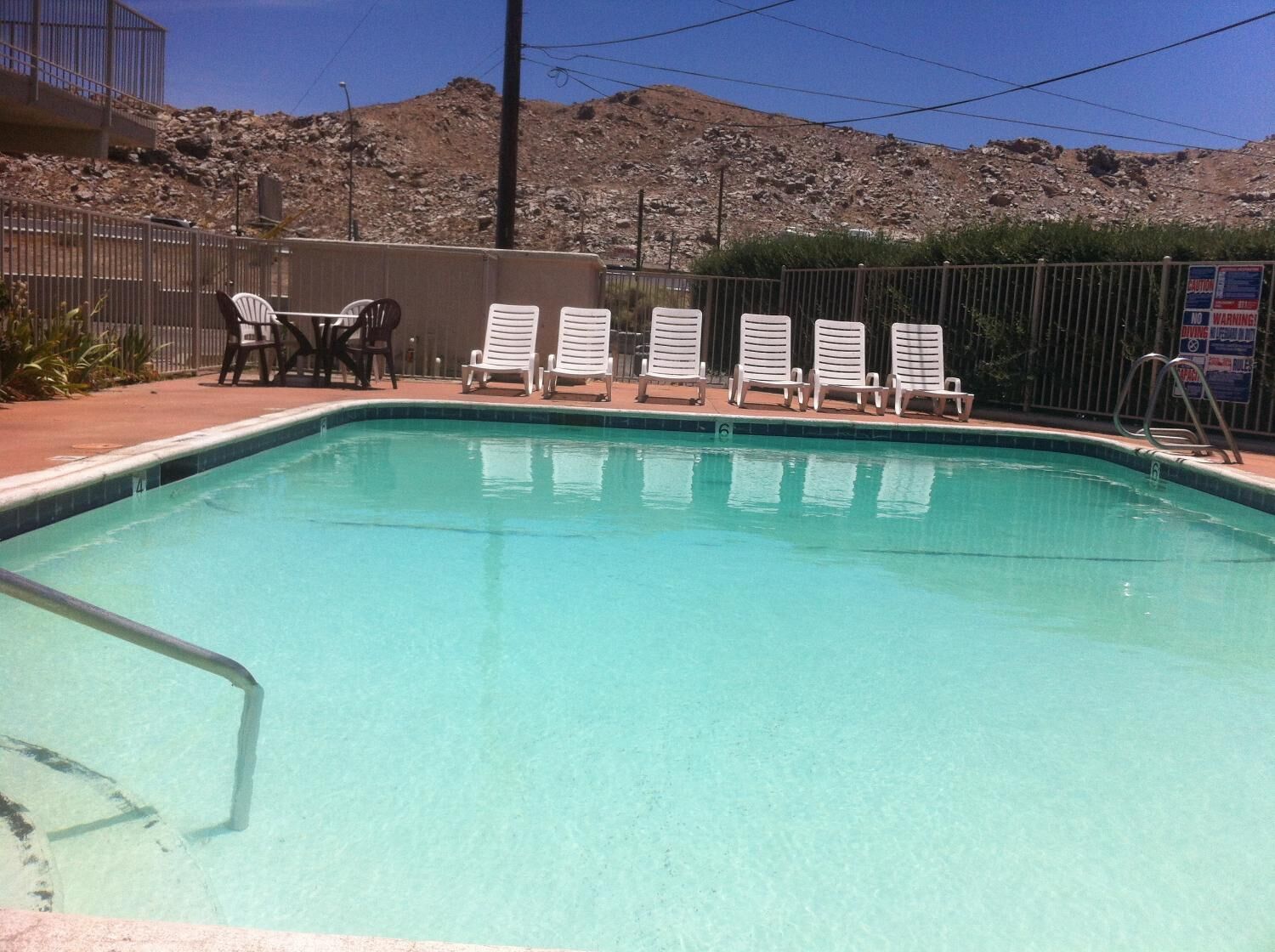 A swimming pool with white lounge chairs and a metal fence.
