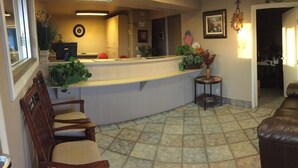 A reception area with a counter, chairs, a brown leather couch, and a tiled floor. - Hilltop Inn & Suites (Victorville)