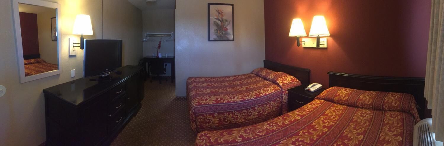 Habitación de hotel con dos camas, un escritorio con una silla, un televisor y dos lámparas fijadas a la pared.