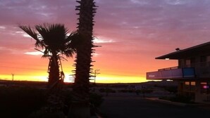 A sunset with palm trees and a building with a signboard. - Hilltop Inn & Suites (Victorville)