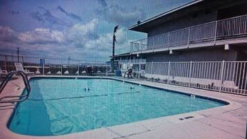 A swimming pool with a diving board, surrounded by a fenced area and a building with a balcony.