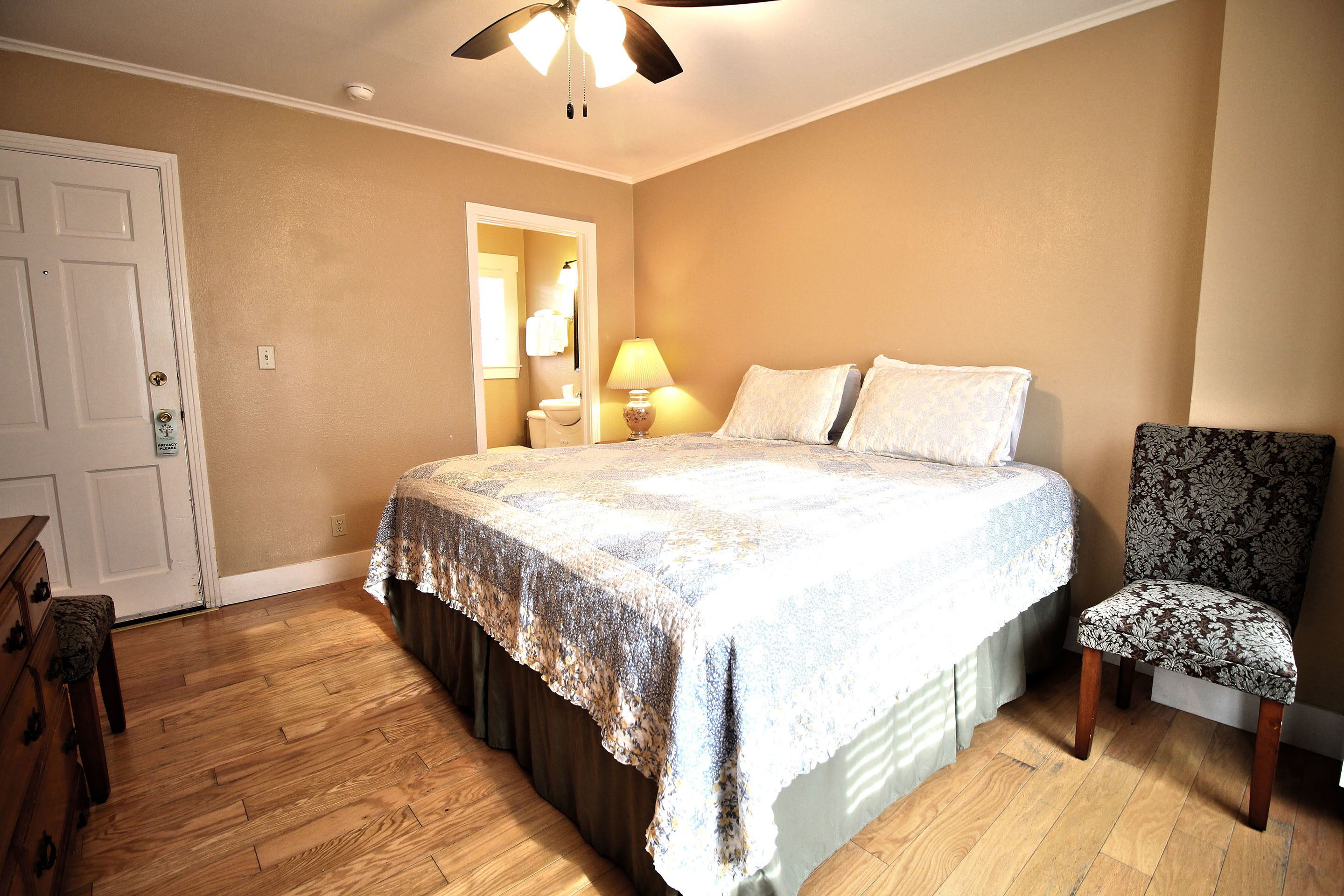 A bedroom with a bed, a chair, a dresser, and a ceiling fan.