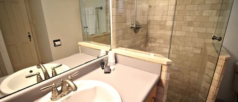 A bathroom with two sinks, a mirror, and a glass-enclosed shower.