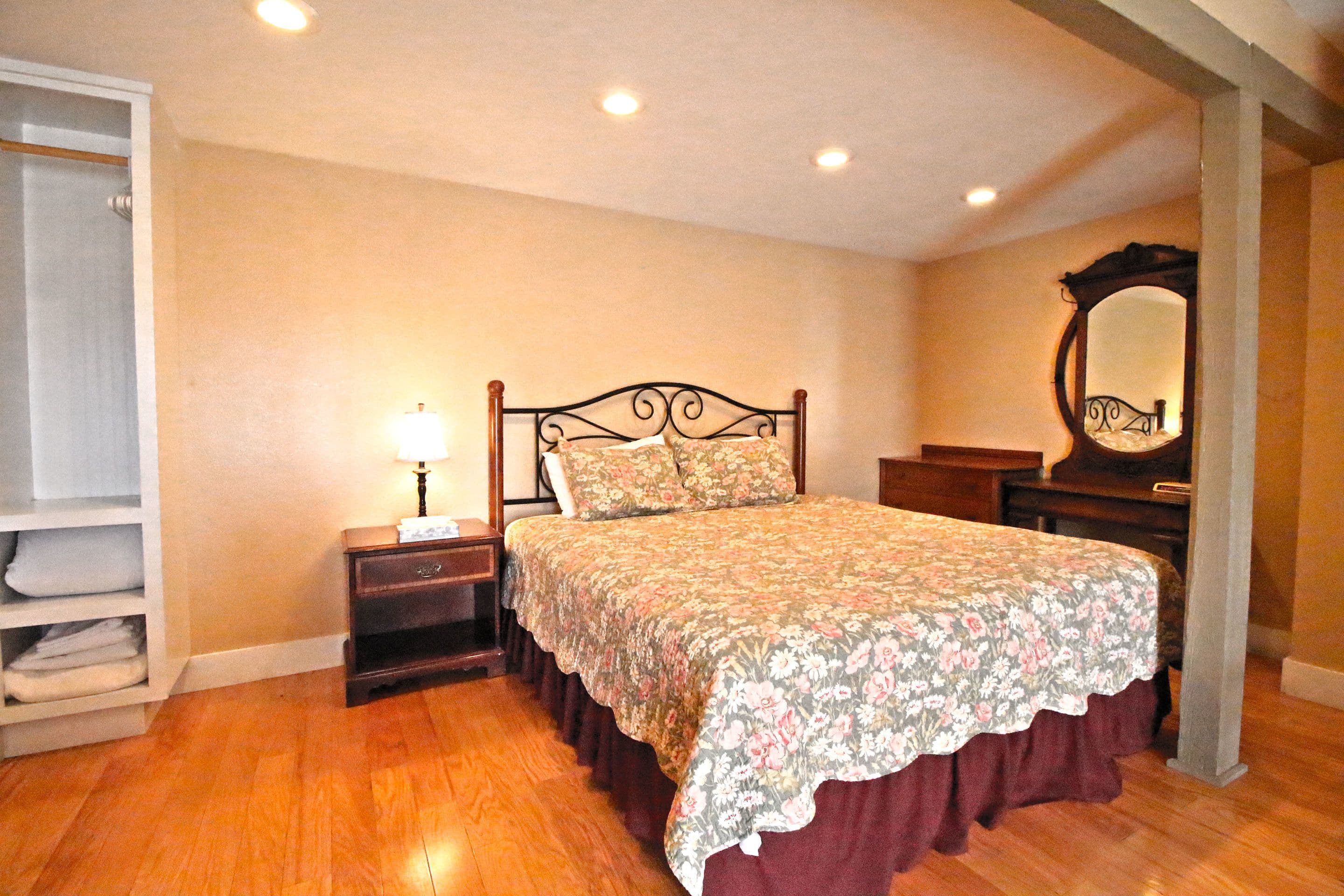 Un dormitorio con cama de madera, mesita de noche, lámpara, armario y espejo.