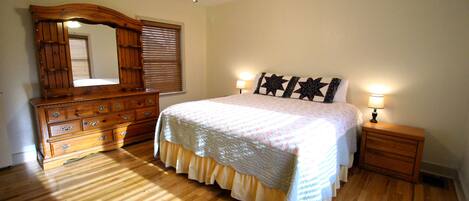 A bedroom with a wooden dresser, a bed with a white bedspread, two bedside lamps, and a ceiling fan.