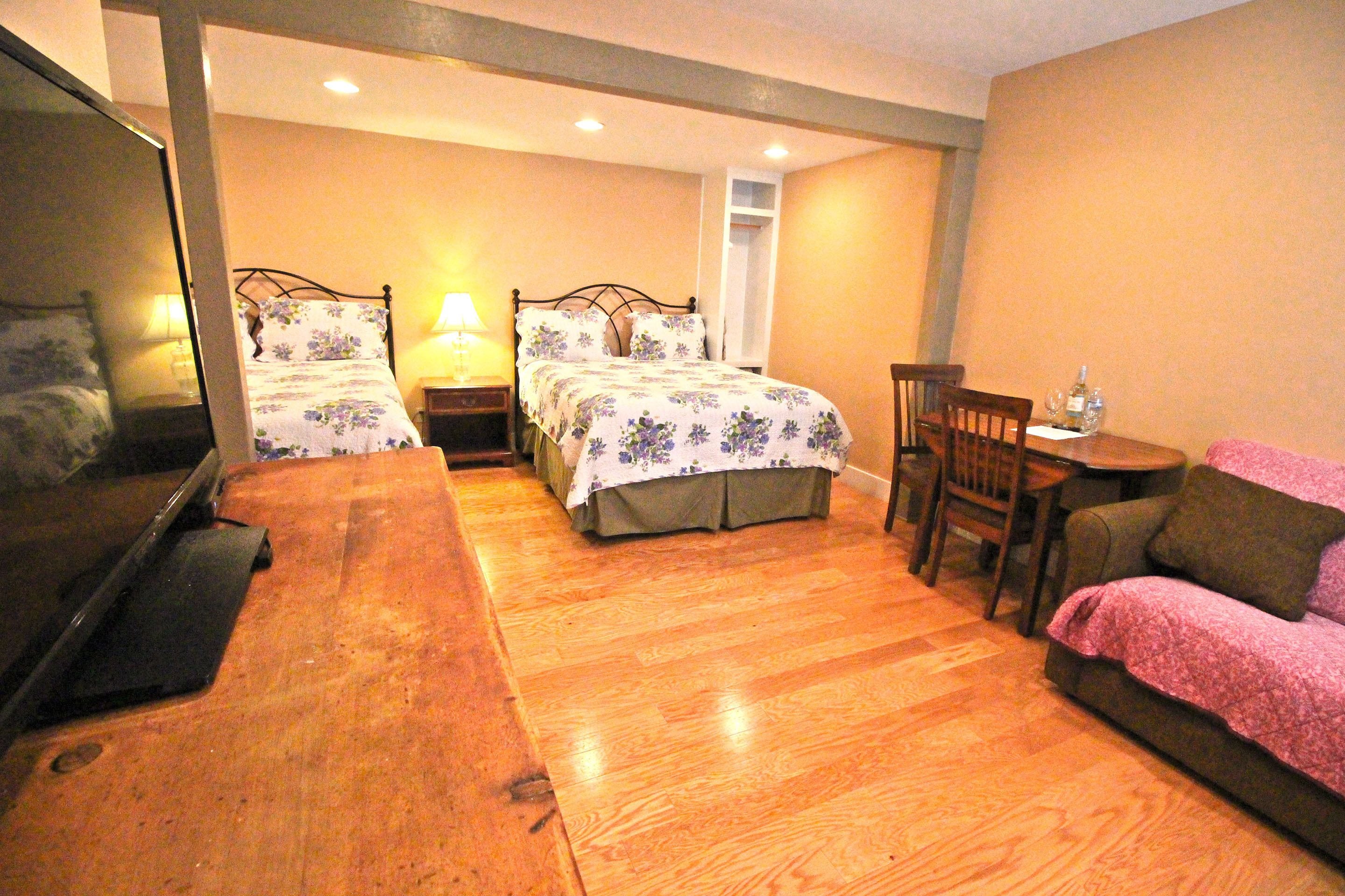 A bedroom with two beds, a wooden dresser, a chair, and a small table with a bottle.