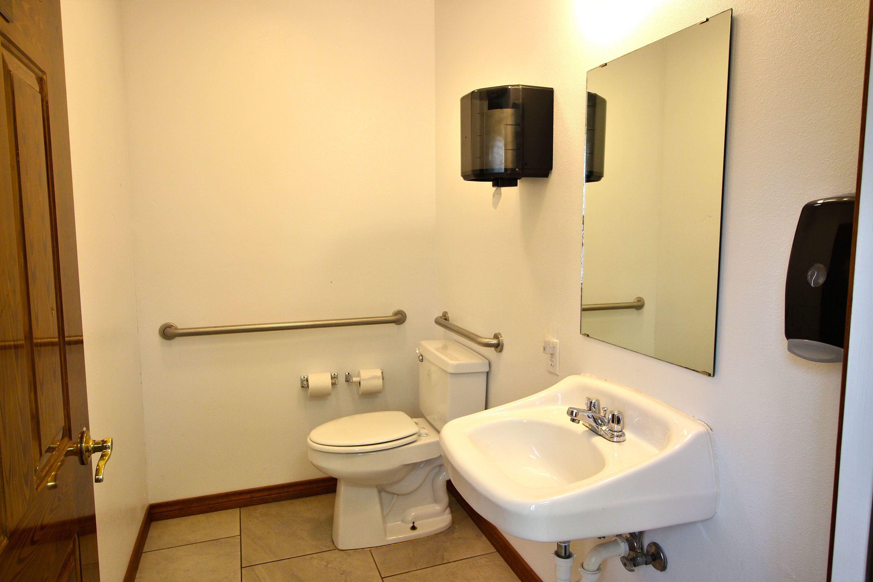 Une petite salle de bain équipée de toilettes, d’un lavabo et d’un distributeur de gel hydroalcoolique.