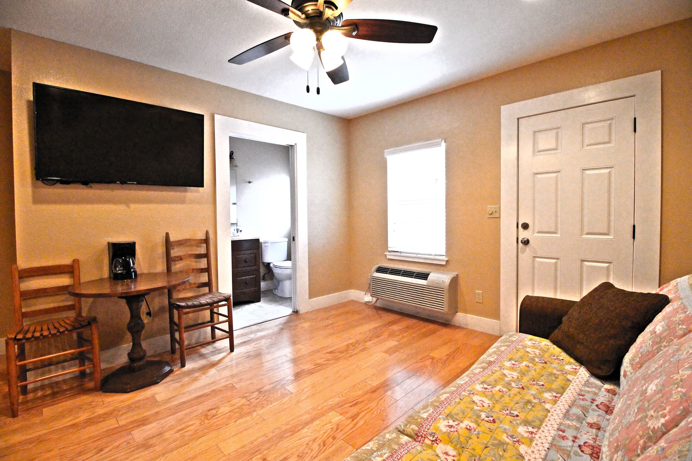 A bedroom with a bed, a ceiling fan, a TV mounted on the wall, and a door.