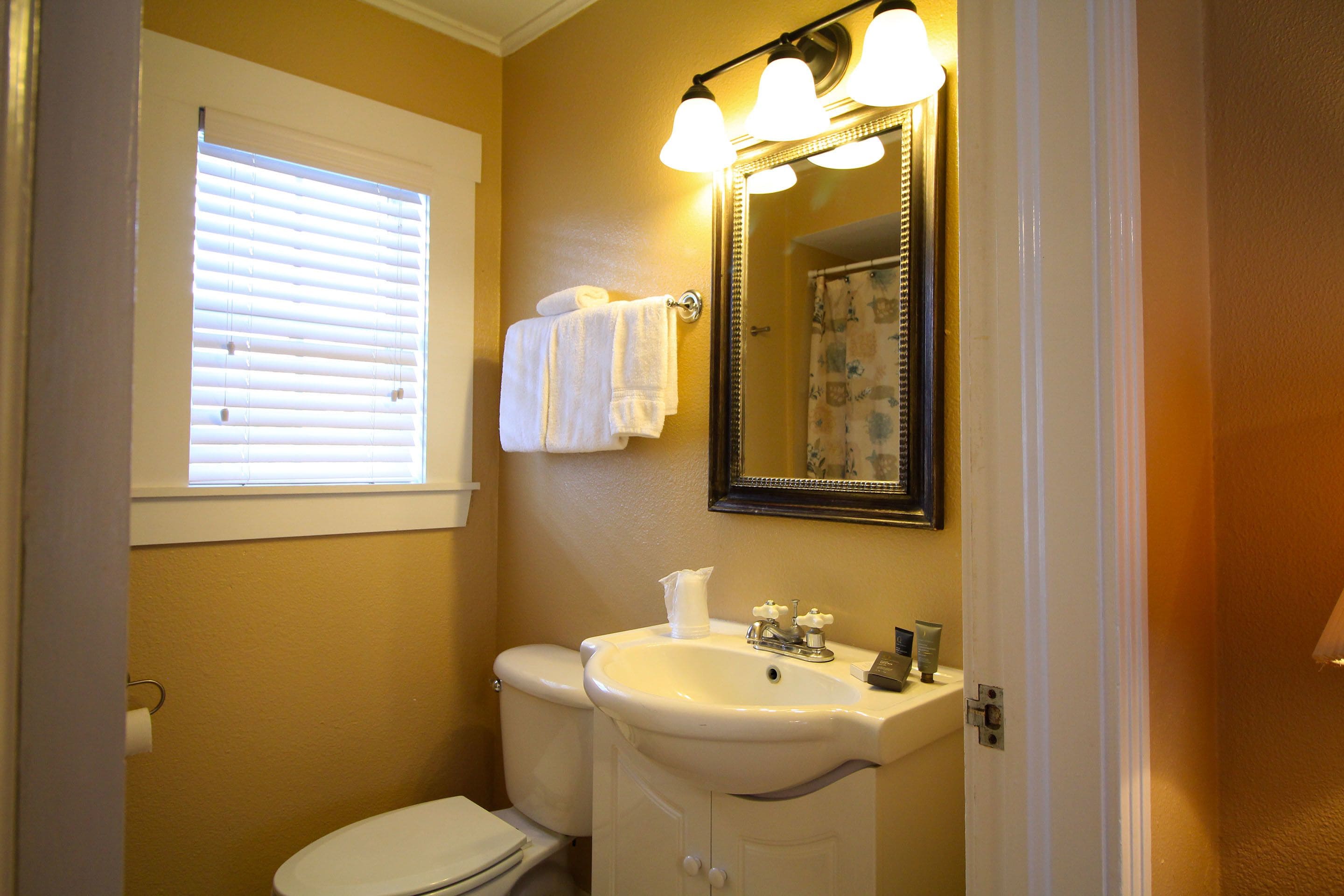 A bathroom with a toilet, sink, and a mirror with lights.