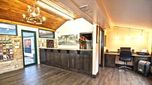 A reception area with a wooden ceiling, a chandelier, a reception desk, a chair, and a computer.