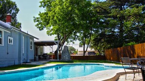 A backyard with a swimming pool, stone patio, and outdoor furniture.