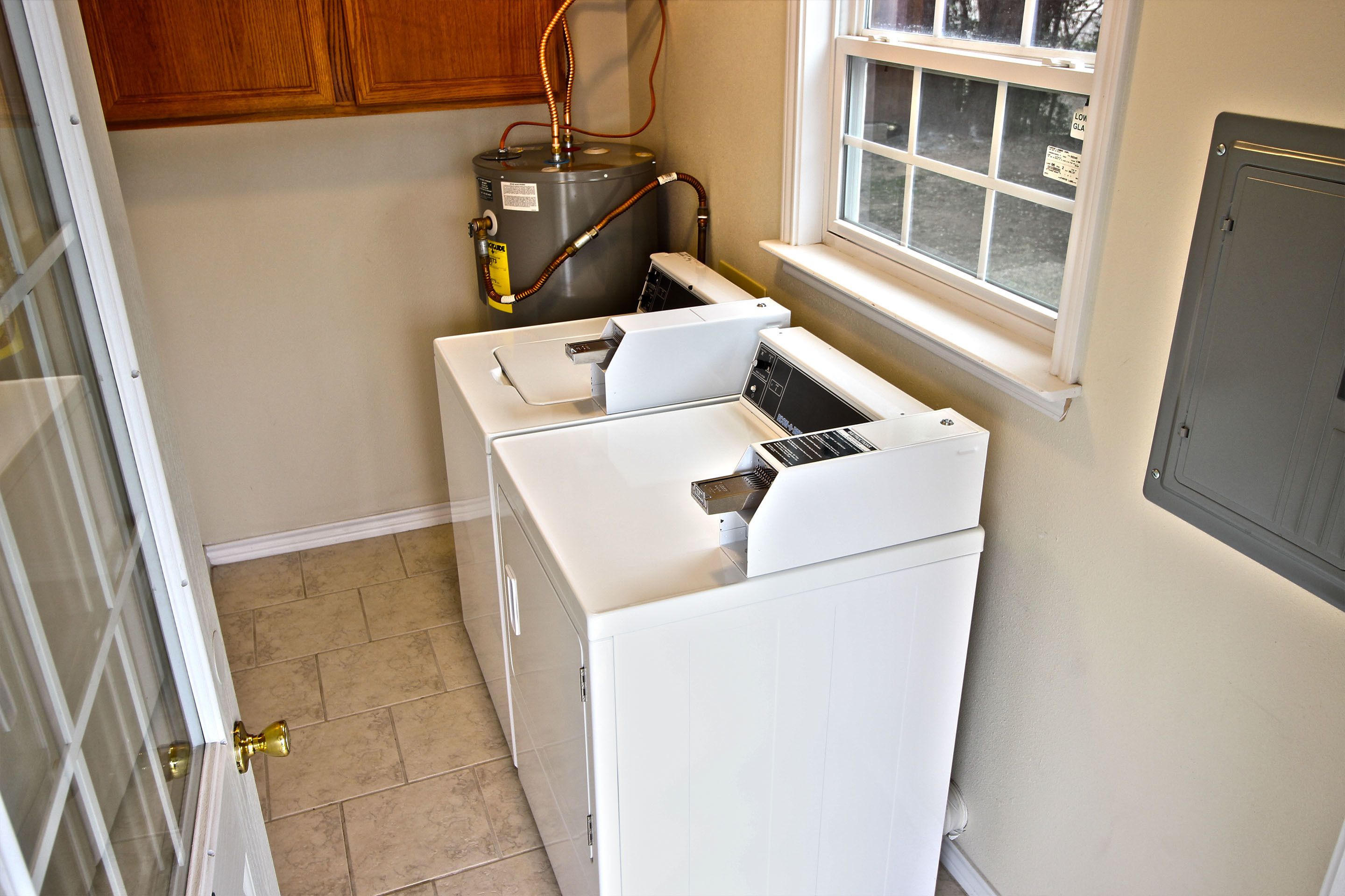 A laundry room with two white washing machines, a water heater, and a window with a view of the outside.
