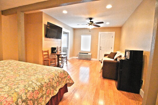 A bedroom with a bed, a desk, a chair, a television, and a ceiling fan.