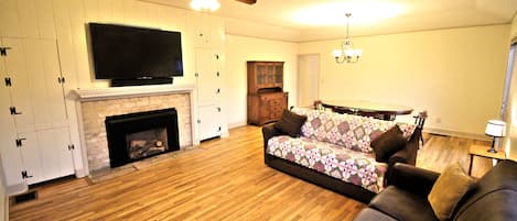 A living room with a fireplace, a sofa, a television, and a ceiling fan.