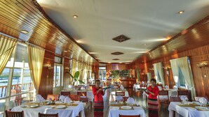 A restaurant with wooden paneling, white tablecloths, and a view of the water.