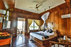 A wooden-paneled room with a bed, a television, and a fruit bowl. - Paramount Inle Resort (Nyaungshwe)