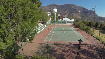 Una cancha de tenis con una red, rodeada por una valla, y un objeto esférico grande al fondo.