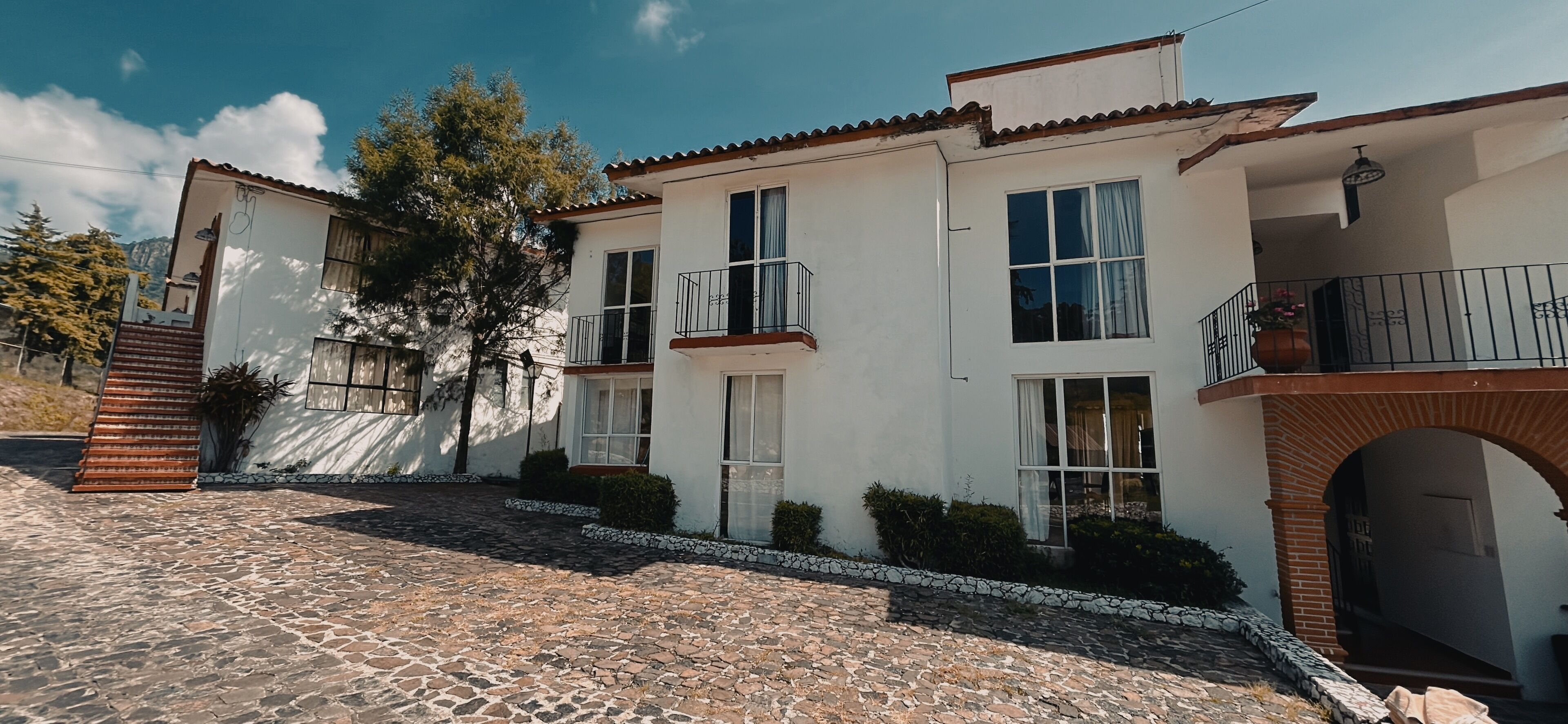 Un edificio de dos plantas con un patio empedrado de piedra, paredes blancas y techo de tejas.