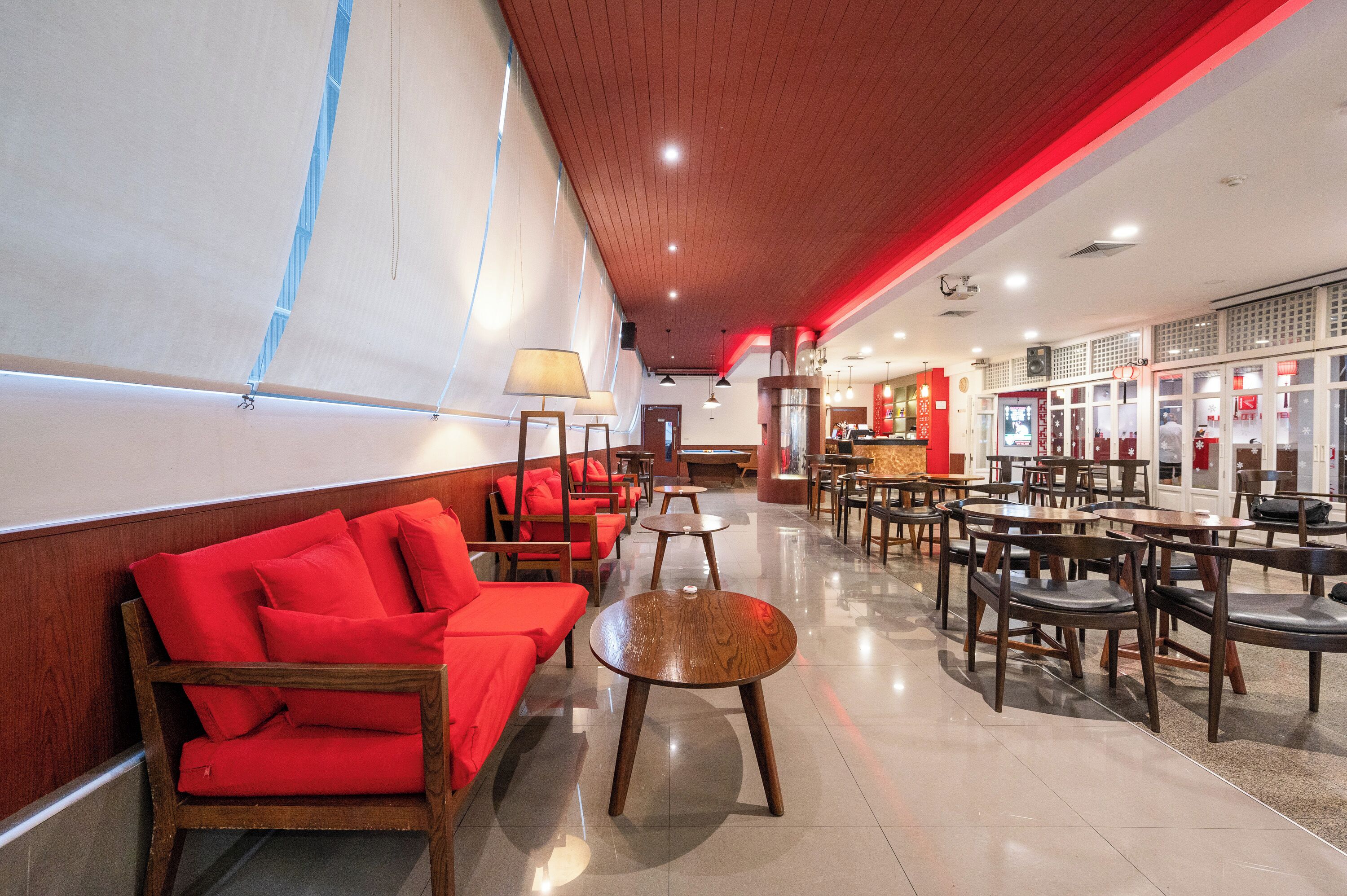 A spacious hotel lobby with a long counter, red seating, and wooden tables.