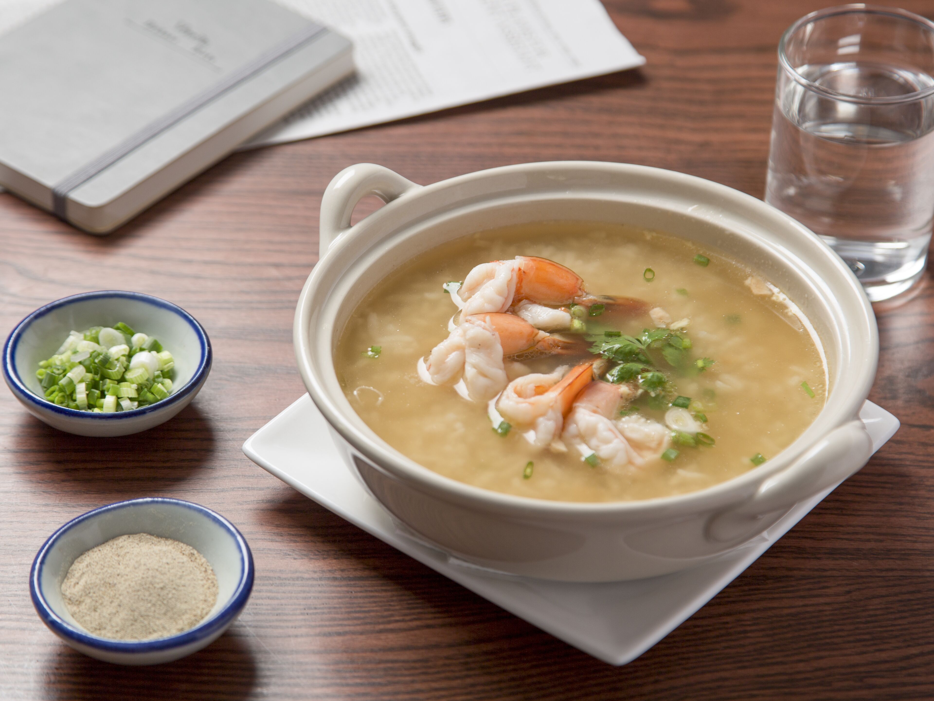 A bowl of soup with shrimp and green onions on a wooden table.
