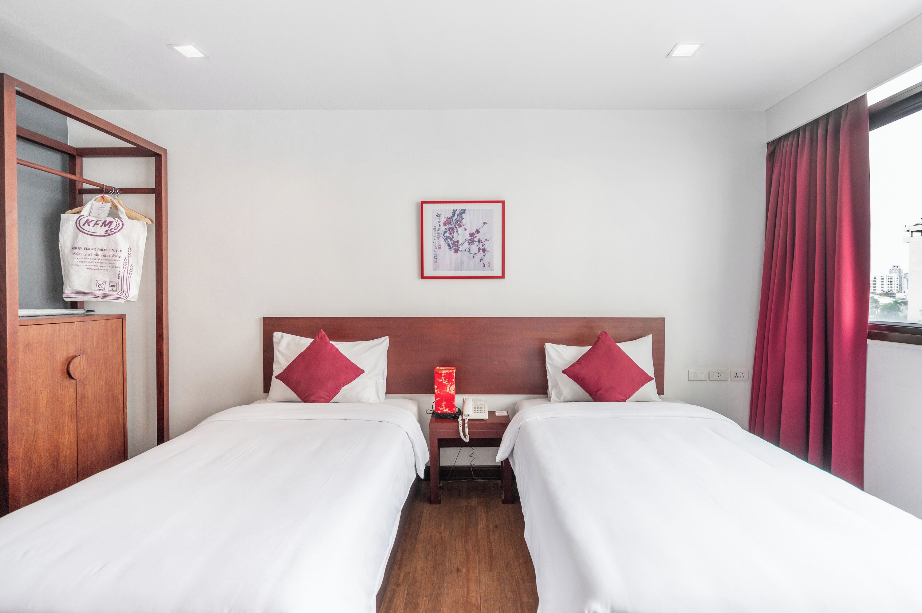 Une chambre d’hôtel avec deux lits, une armoire en bois, une œuvre d’art encadrée au mur et une fenêtre avec des rideaux rouges.