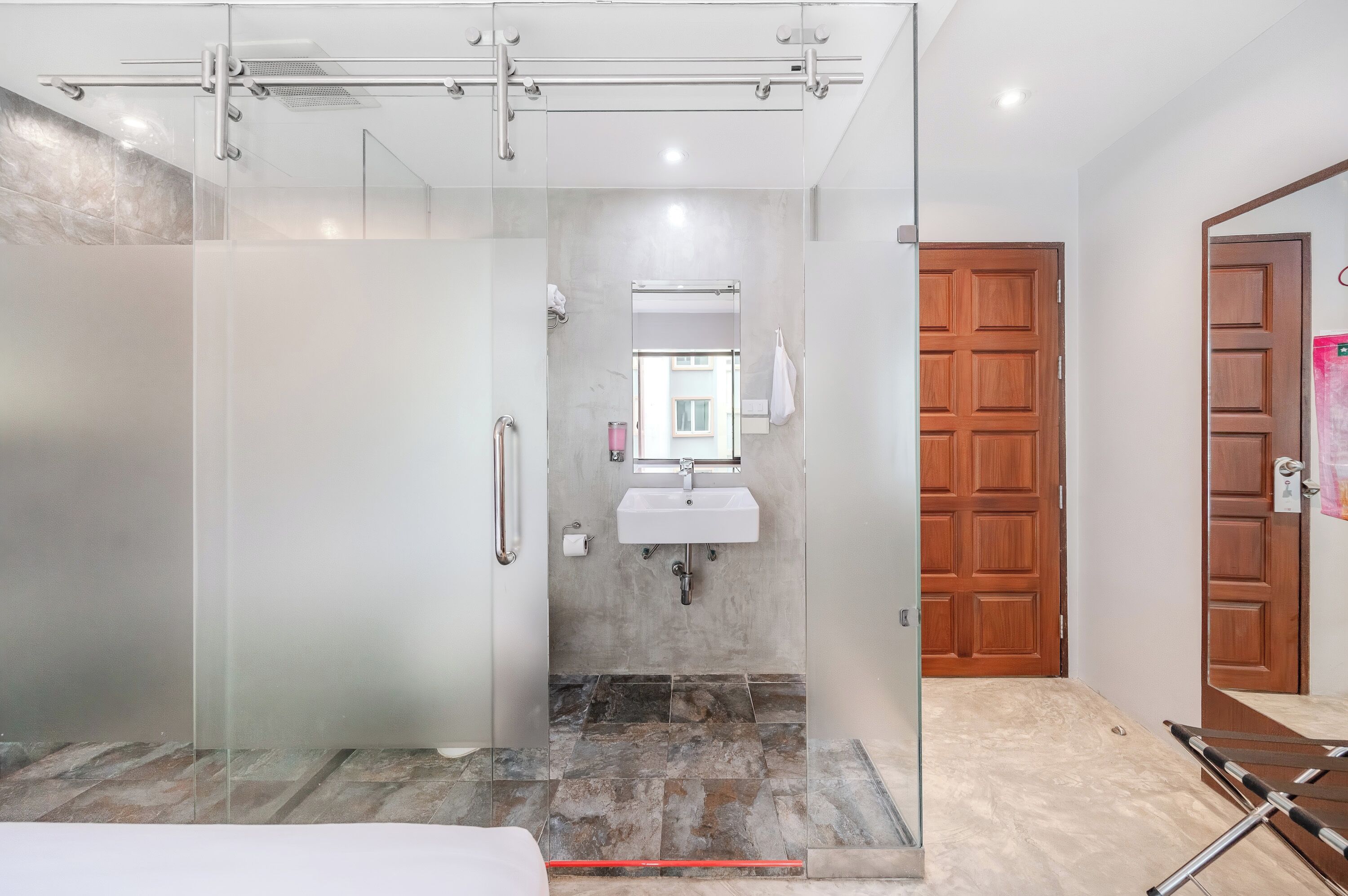 A modern bathroom with a glass shower enclosure, a white sink, and a wooden door.