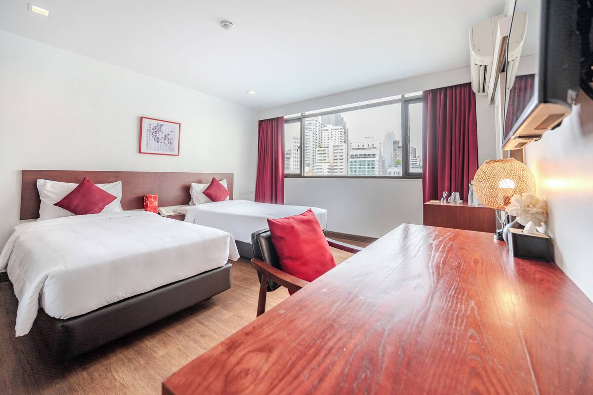 A hotel room with two beds, a wooden desk, a city view, and a framed picture on the wall.