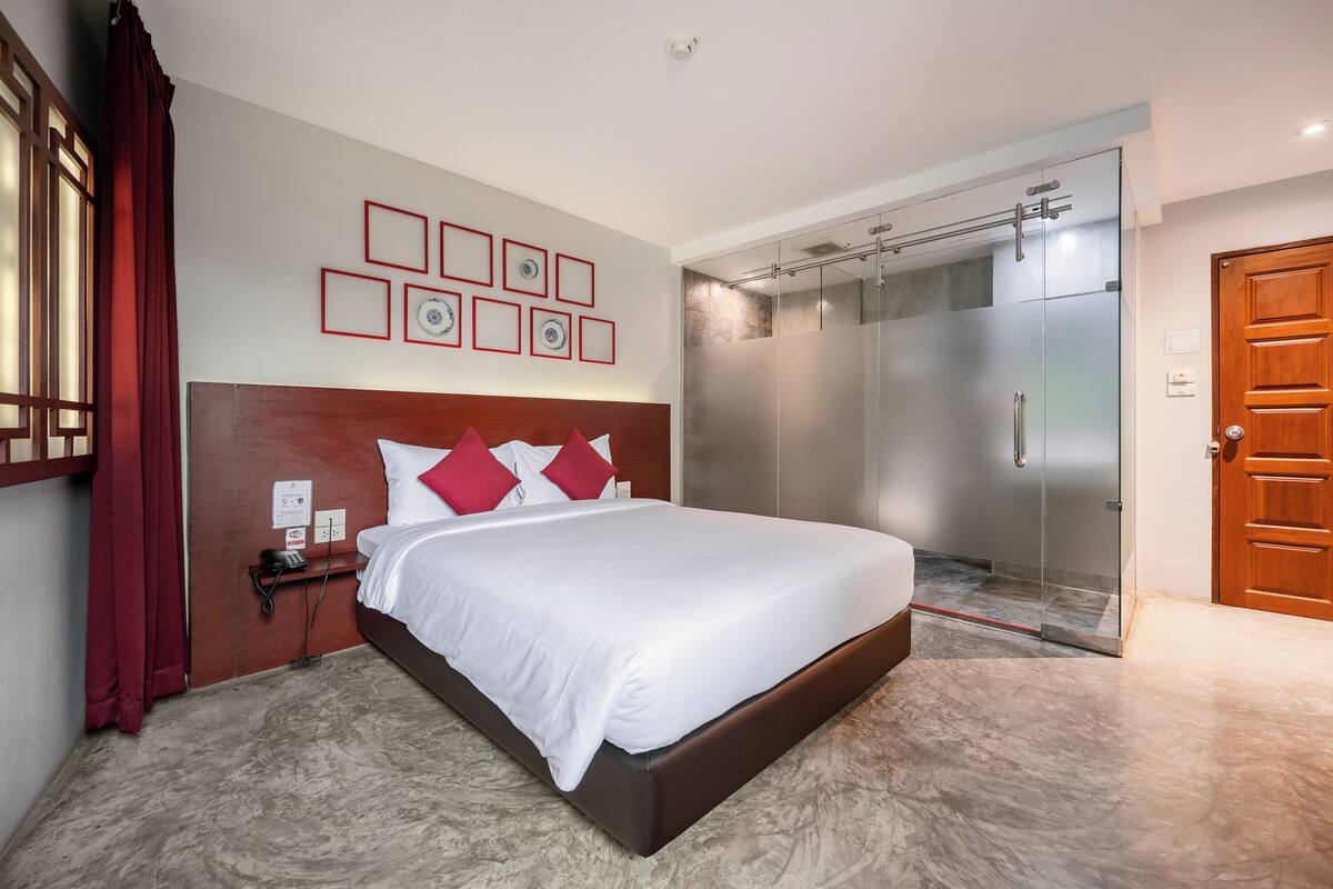 A hotel room with a large bed, a wooden headboard, a glass shower enclosure, and a wooden door.