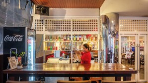 A bar area with a Coca-Cola refrigerator, shelves of liquor bottles, and a person serving.