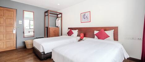 Habitación de hotel con dos camas, cabeceros de madera, un armario de madera, un espejo, un cuadro enmarcado y una lámpara roja.