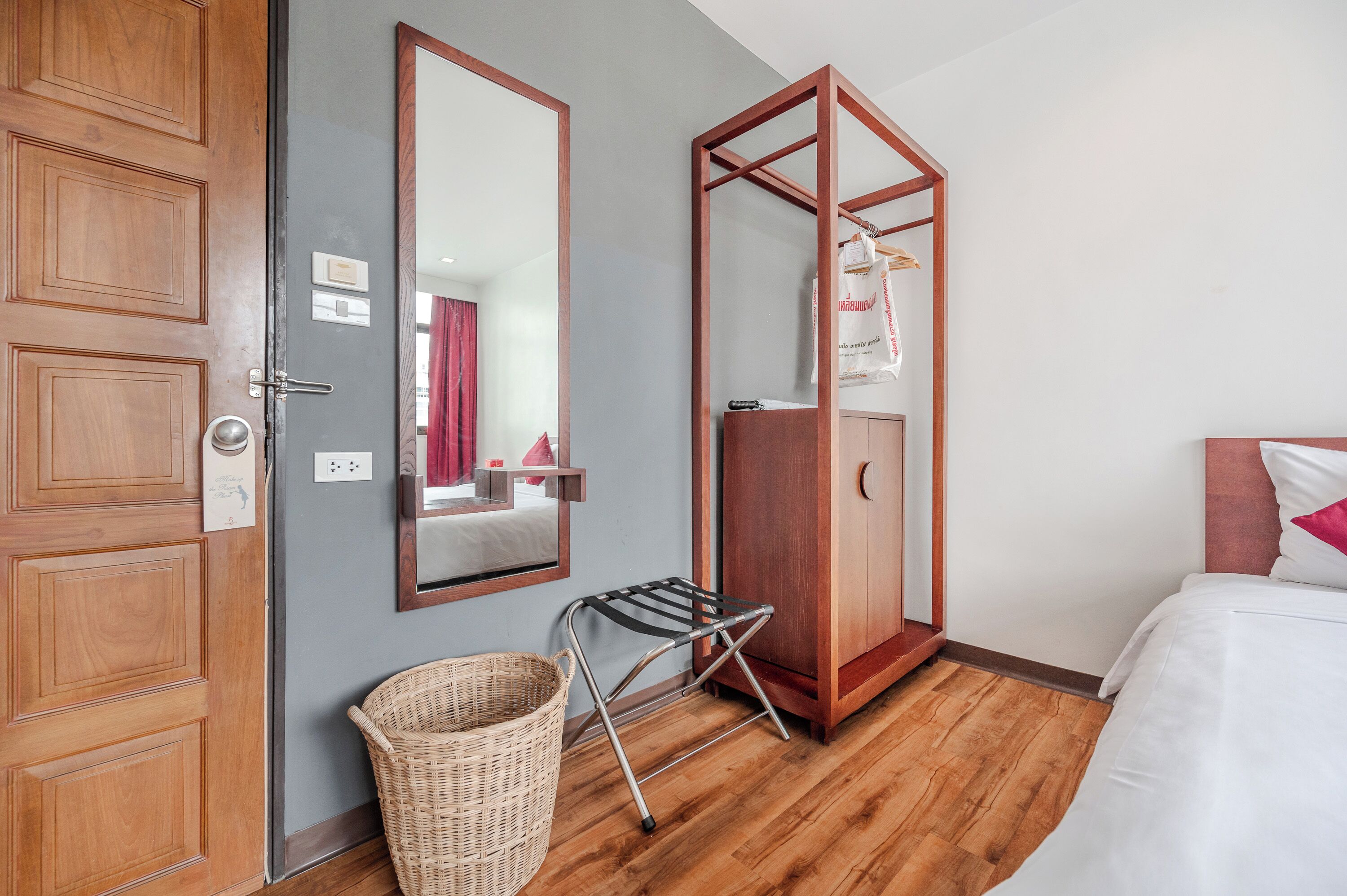 A hotel room with a wooden wardrobe, a mirror, a wicker basket, and a bed with white bedding.
