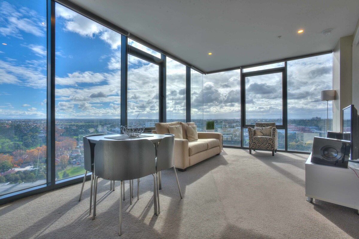 A spacious room with large windows, a sofa, a dining table, and a chair.