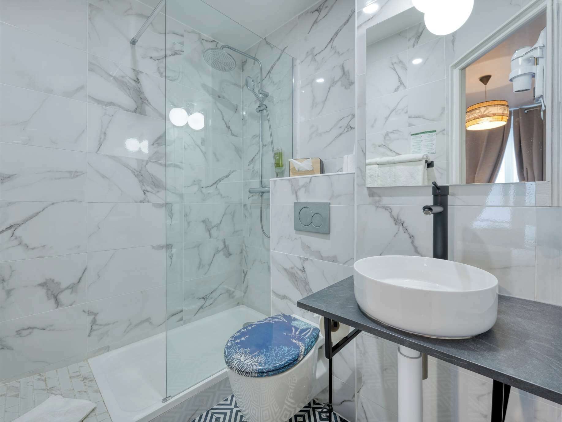 A modern bathroom with a glass-enclosed shower, a white sink on a dark countertop, and a patterned floor.