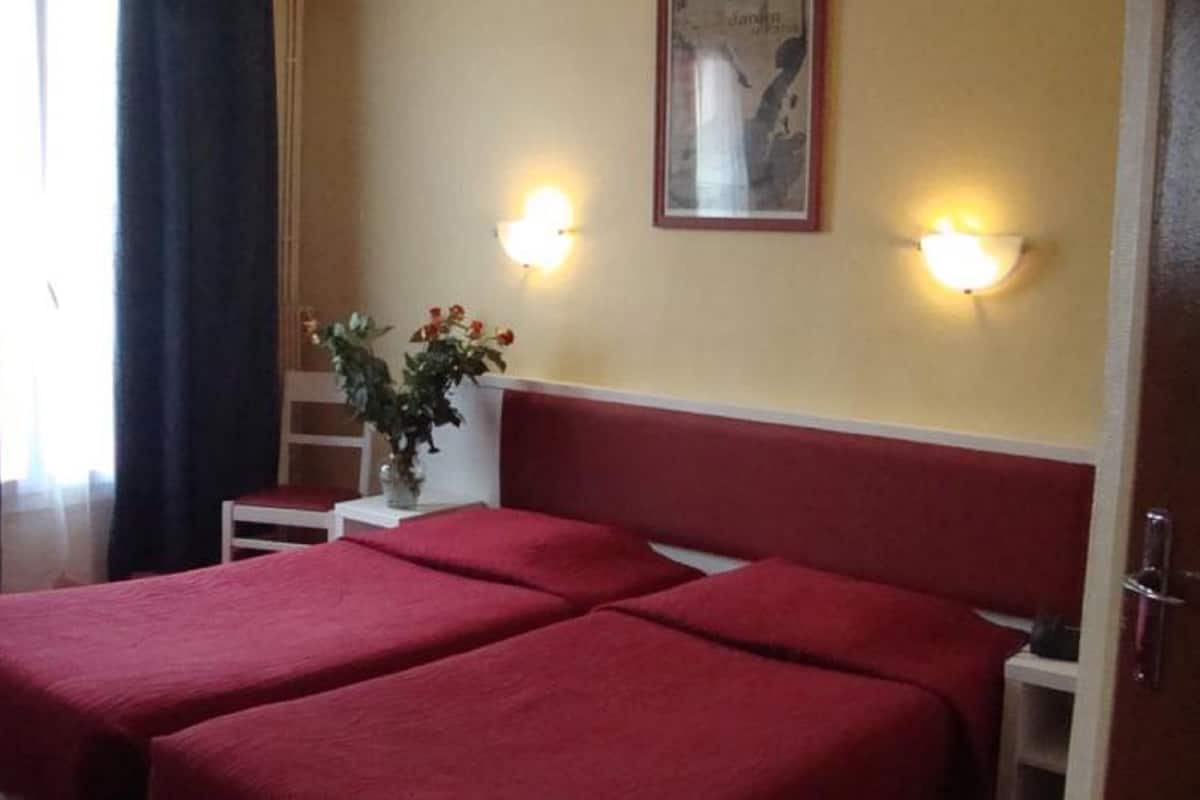 A hotel room with two beds, a nightstand, a vase with flowers, and wall-mounted lights.