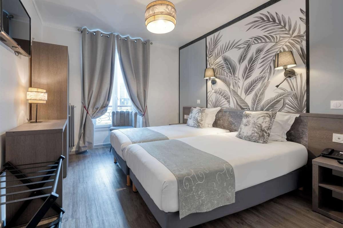 A modern hotel room with a large bed, two bedside lamps, a view of the city, and a large mirror with a leaf pattern.