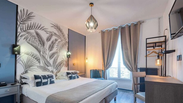 A modern bedroom with a large bed, a desk, and a view of the outdoors. - Hotel de Belfort (Paris)