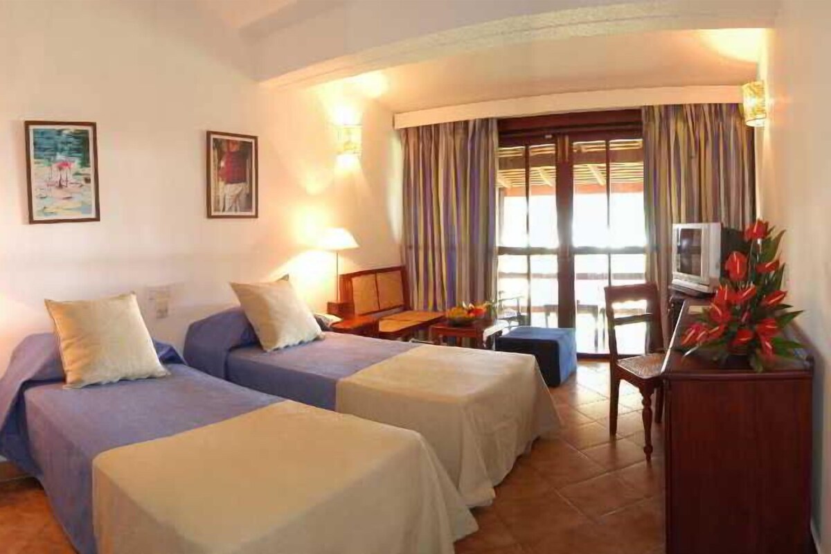A hotel room with two beds, a TV, a desk, and a window with curtains.
