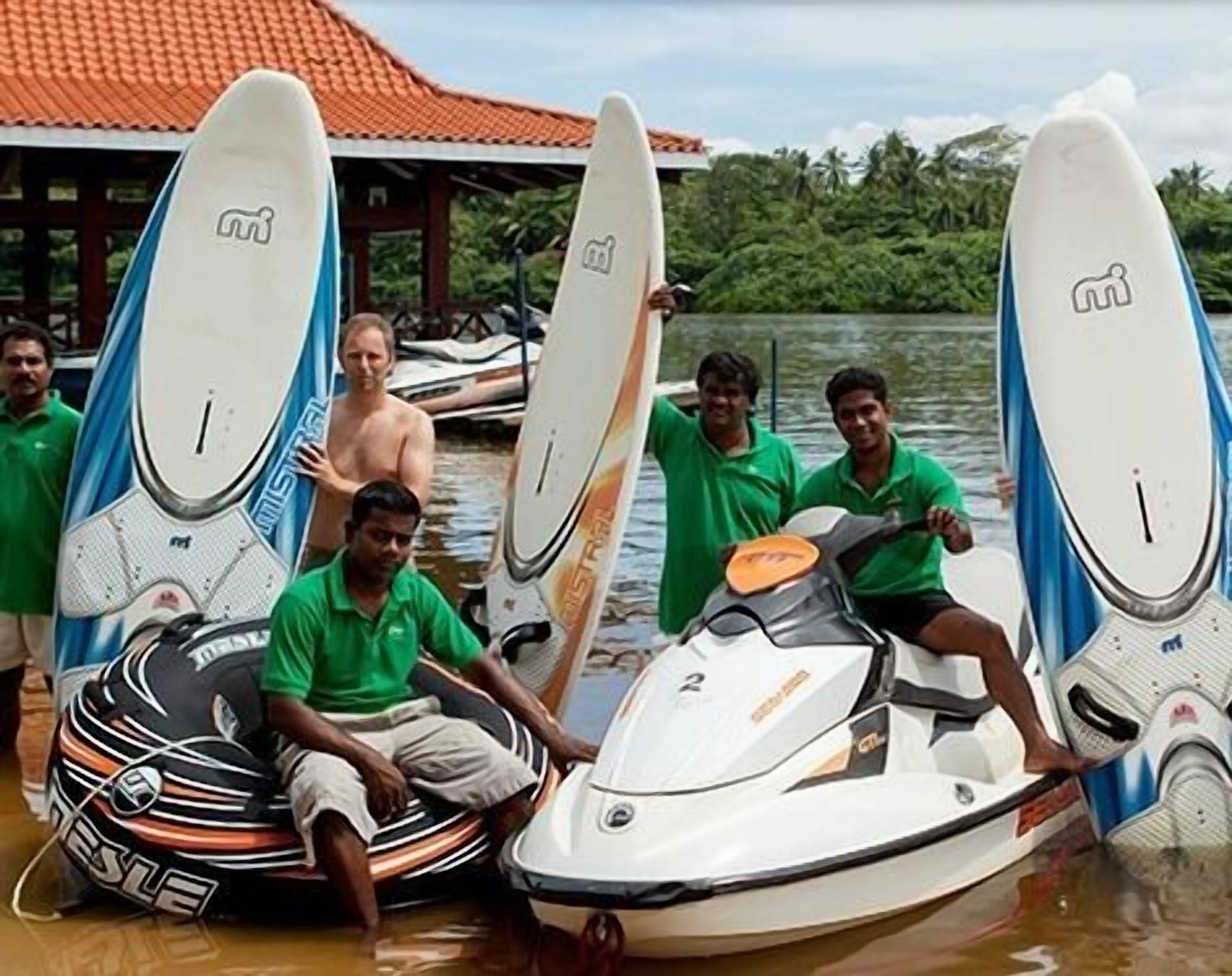A group of people on a jet ski with surfboards, a man in a green shirt, and a woman in a green top.