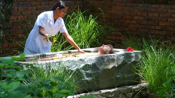 Guests can unwind on a stone platform amidst lush greenery and a brick wall.