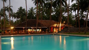 A poolside area with a building that has a tiled roof and a red accent wall. - Club Bentota (Bentota)